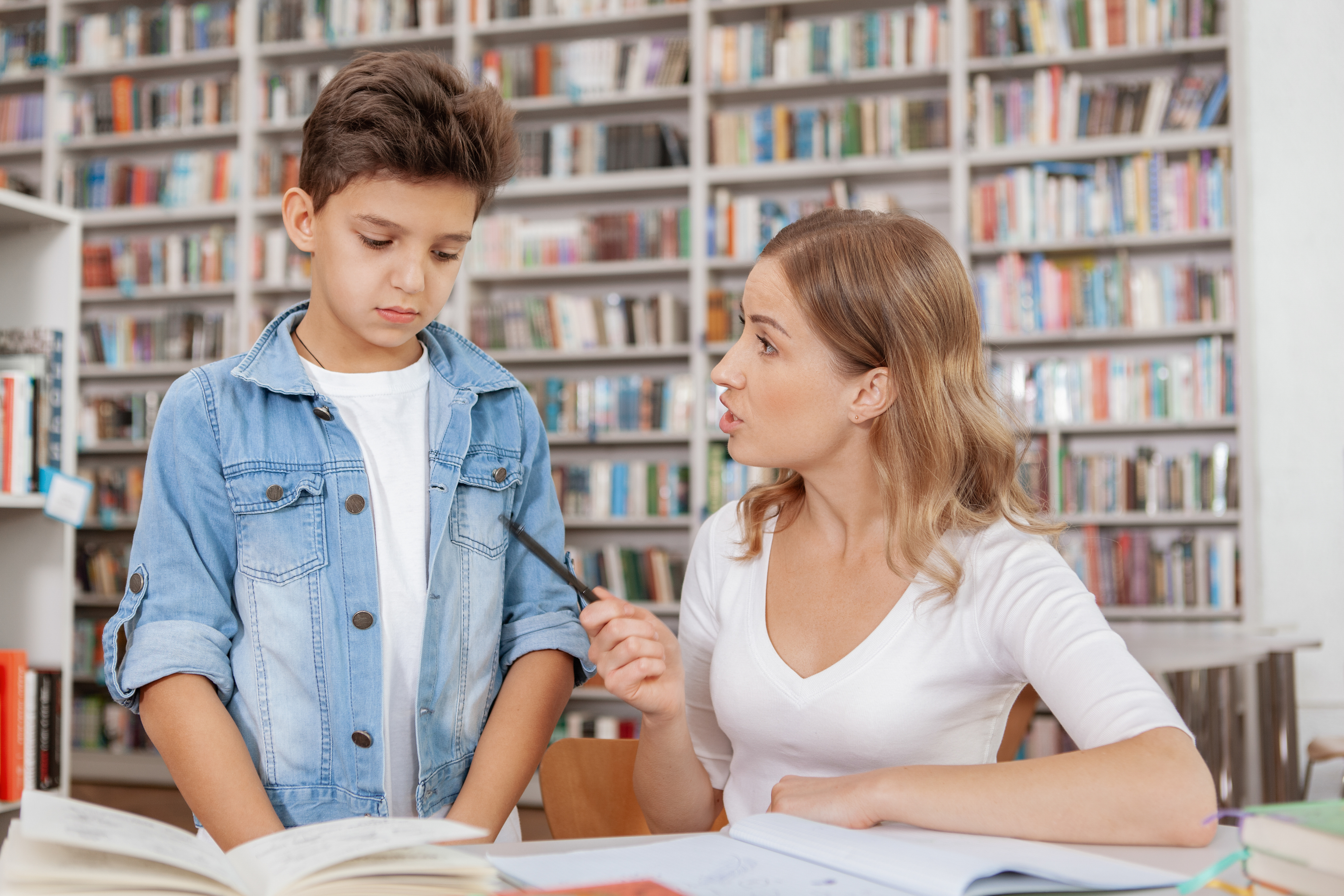 Woman and boy engaged in discussion with open books on the table in a library setting