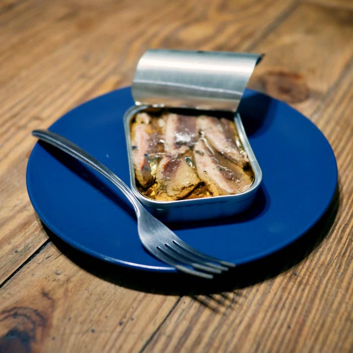 Open tin of sardines on a blue plate with a fork on a wooden table