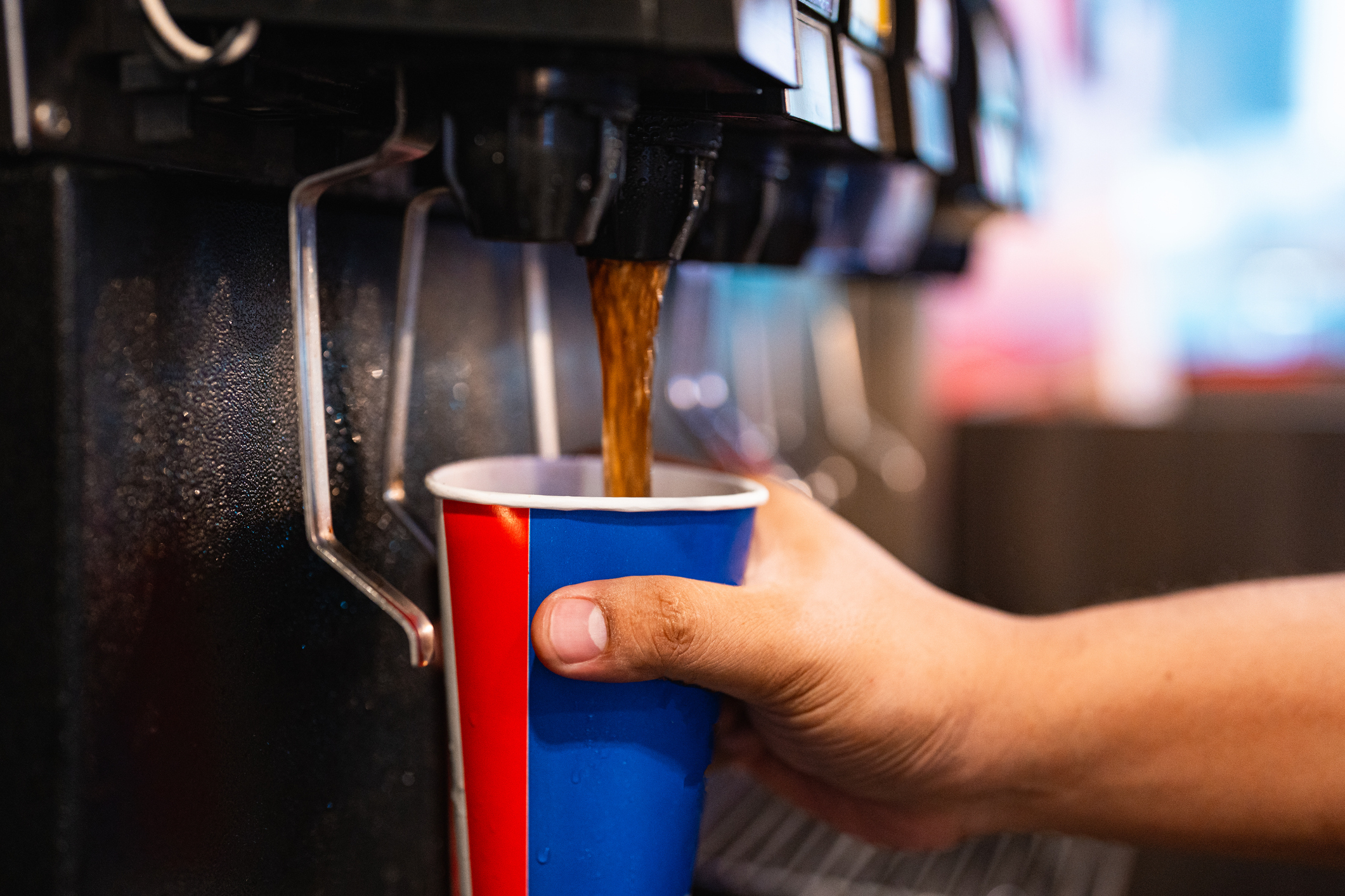 Person filling a red and blue cup with a beverage from a dispenser