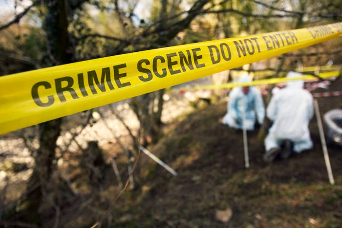 Crime scene tape with forensic experts examining the area behind it