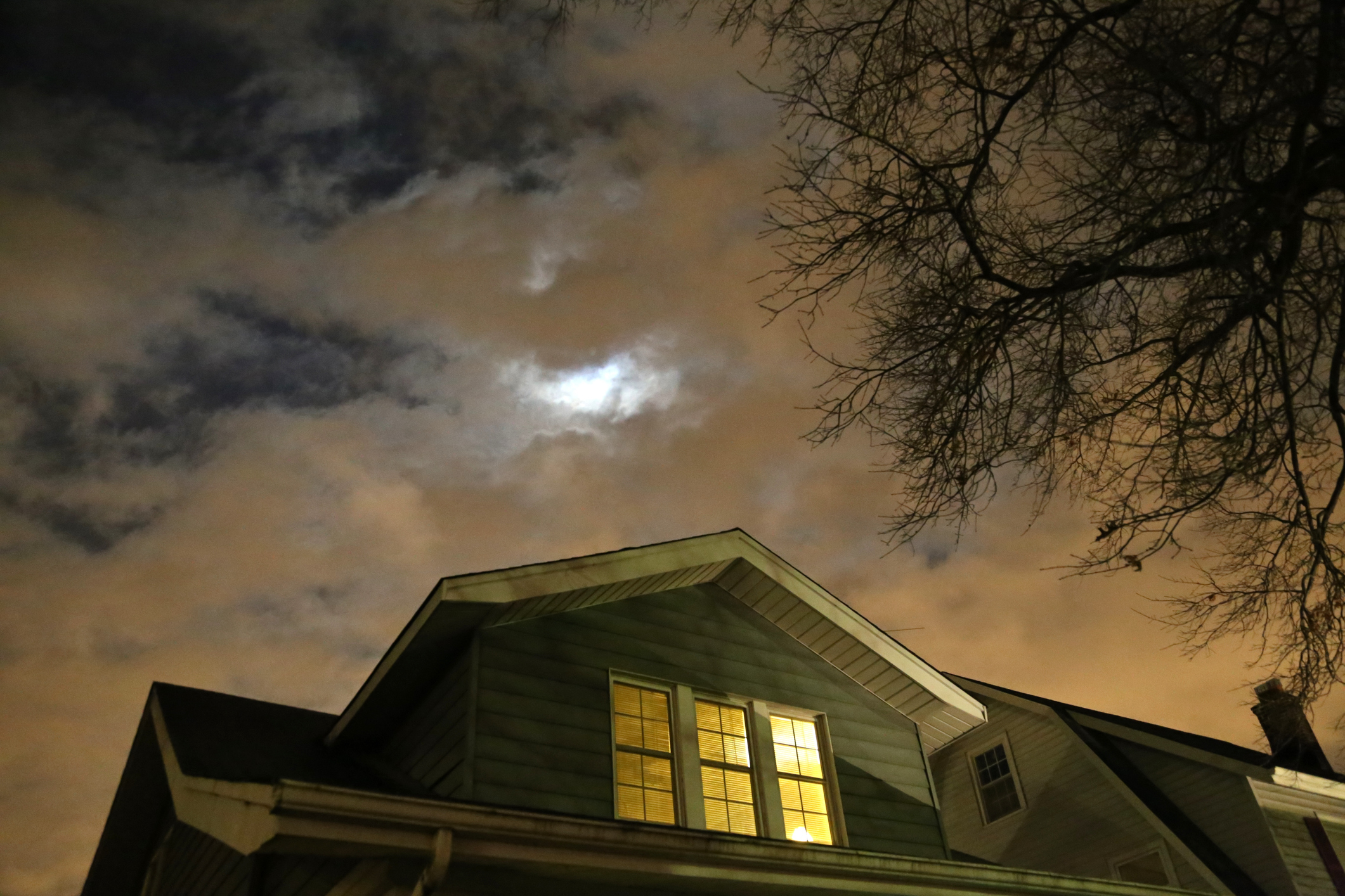 Night sky with clouds partially covering the moon above a house with lit windows