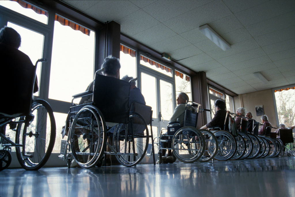 A row of individuals in wheelchairs facing a window in a room, conversing and enjoying the view