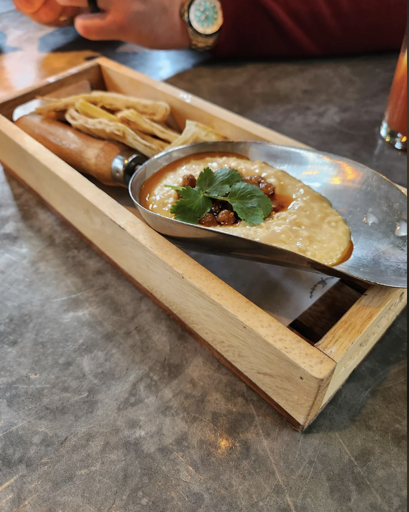 a wooden tray with hummus, pita bread, and crispy onions inside gardening equipment