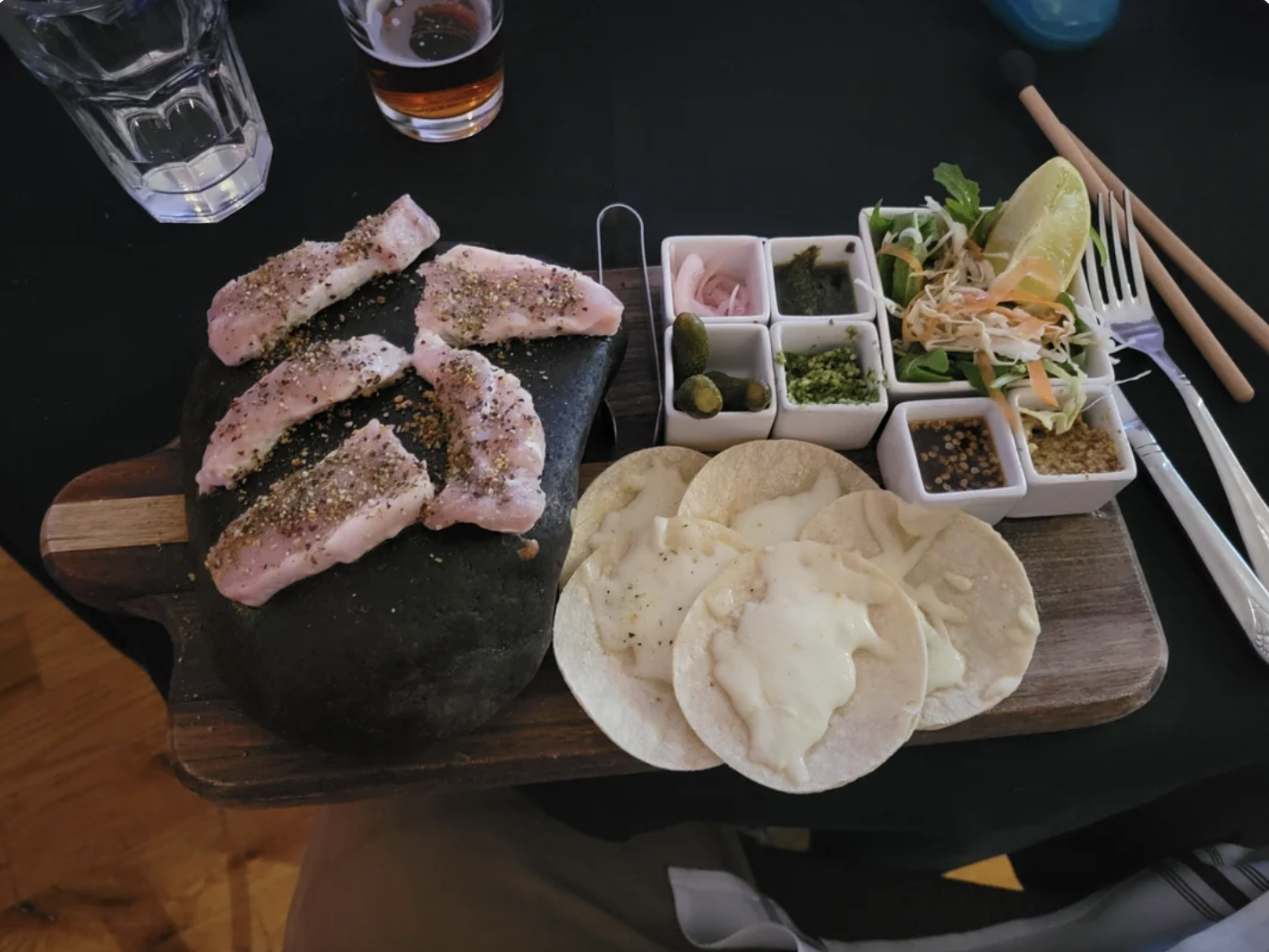 A meal set with chicken, tortillas, and various toppings on a wooden board