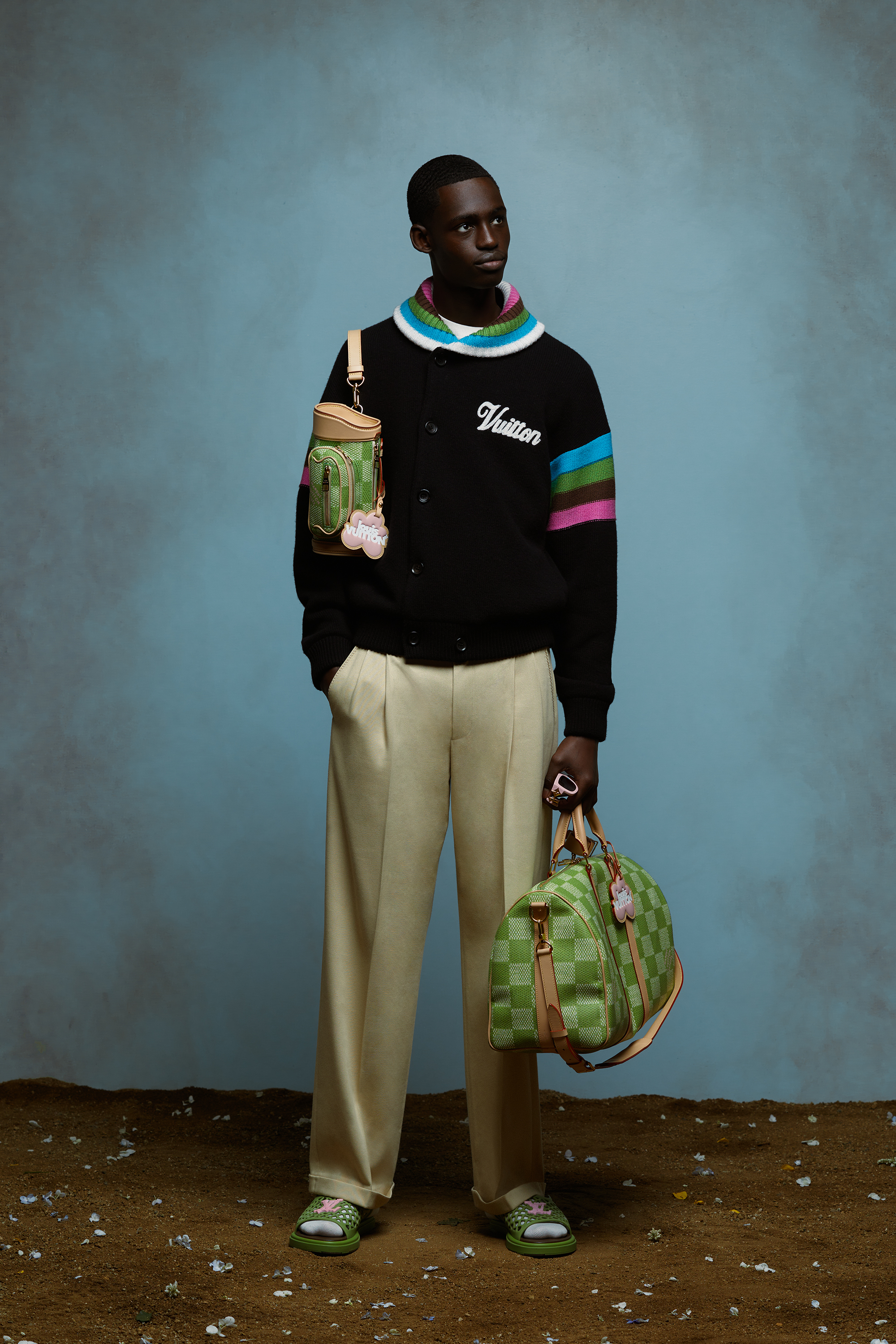Elegant person in a varsity jacket, striped sweater, and trousers holding two stylish bags