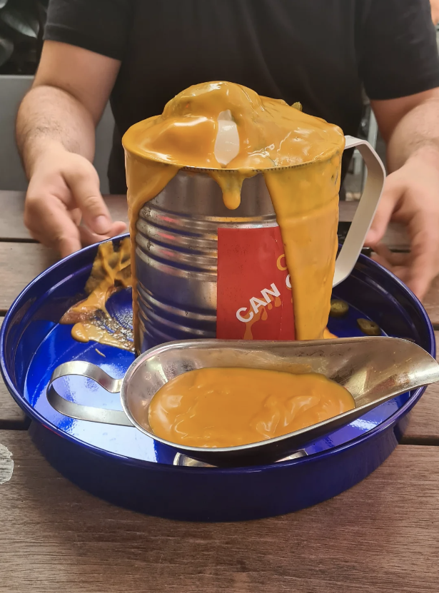 Person at table with overflowing canned cheese product and spoon on blue tray