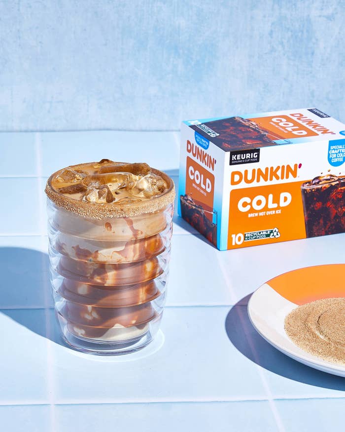Iced coffee in a clear glass next to a Dunkin&#x27; Cold brew box with a plain background