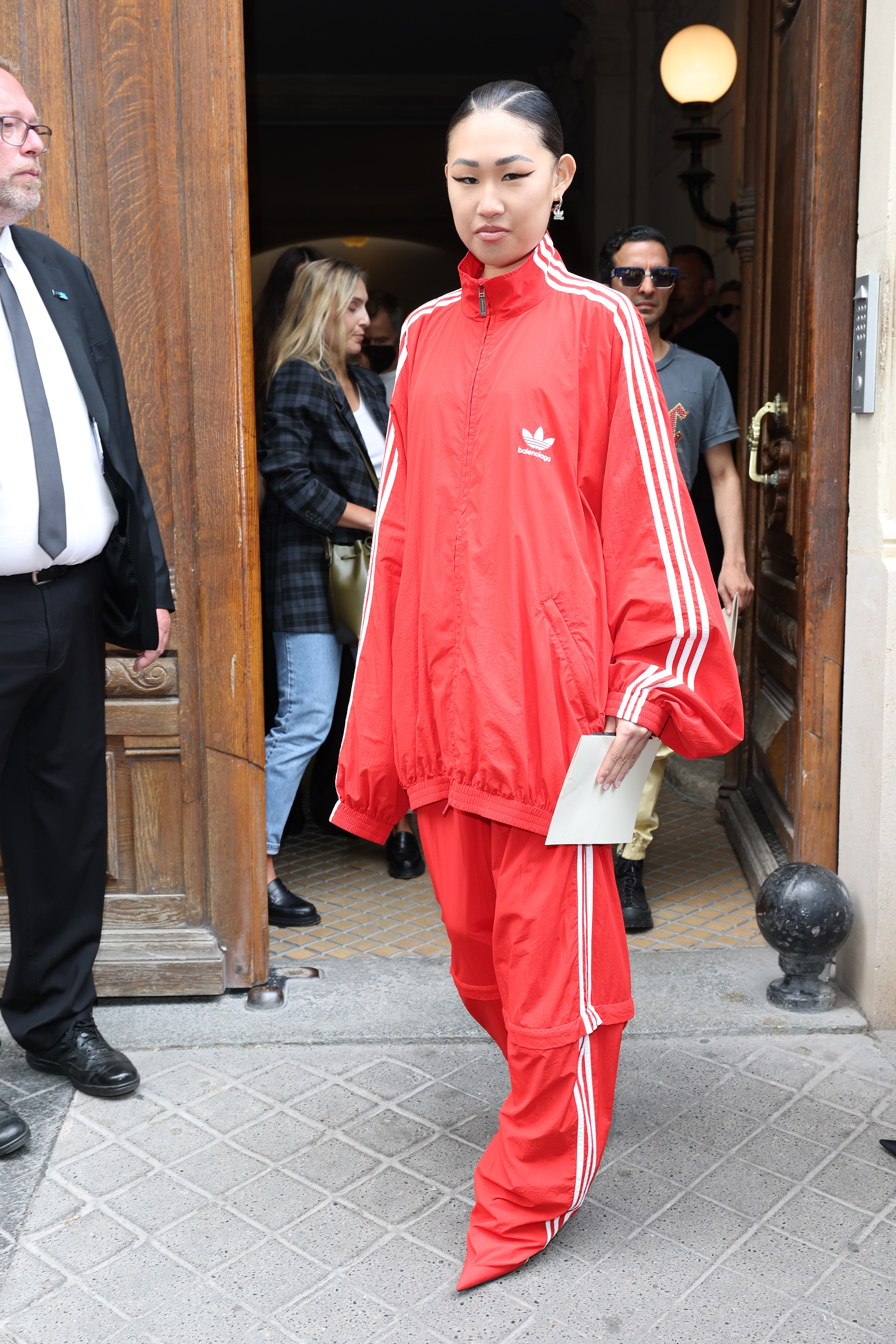 Person in a red designer tracksuit steps out of a building, style focus