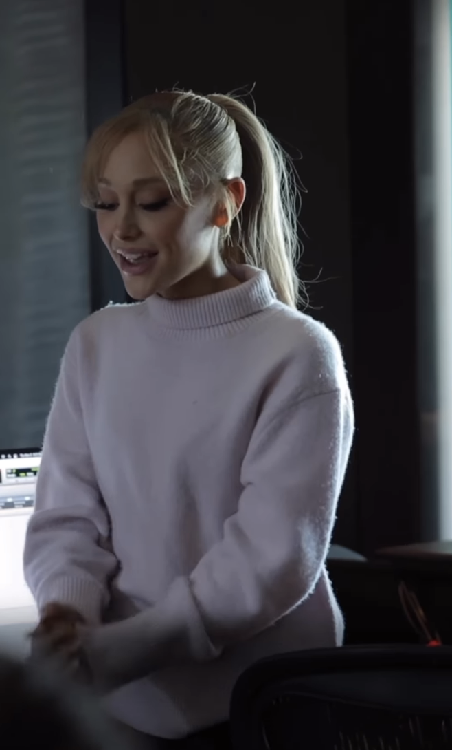 Smiling woman in a turtleneck sweater at a mixing console in a studio