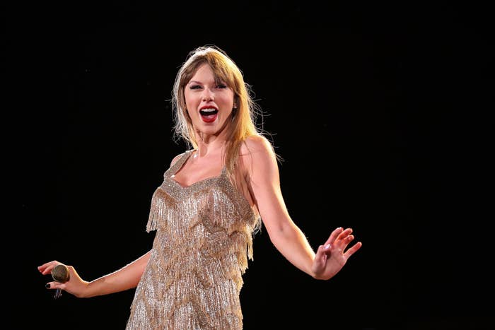 Taylor Swift is onstage singing in a sparkling fringe dress, with a microphone in hand