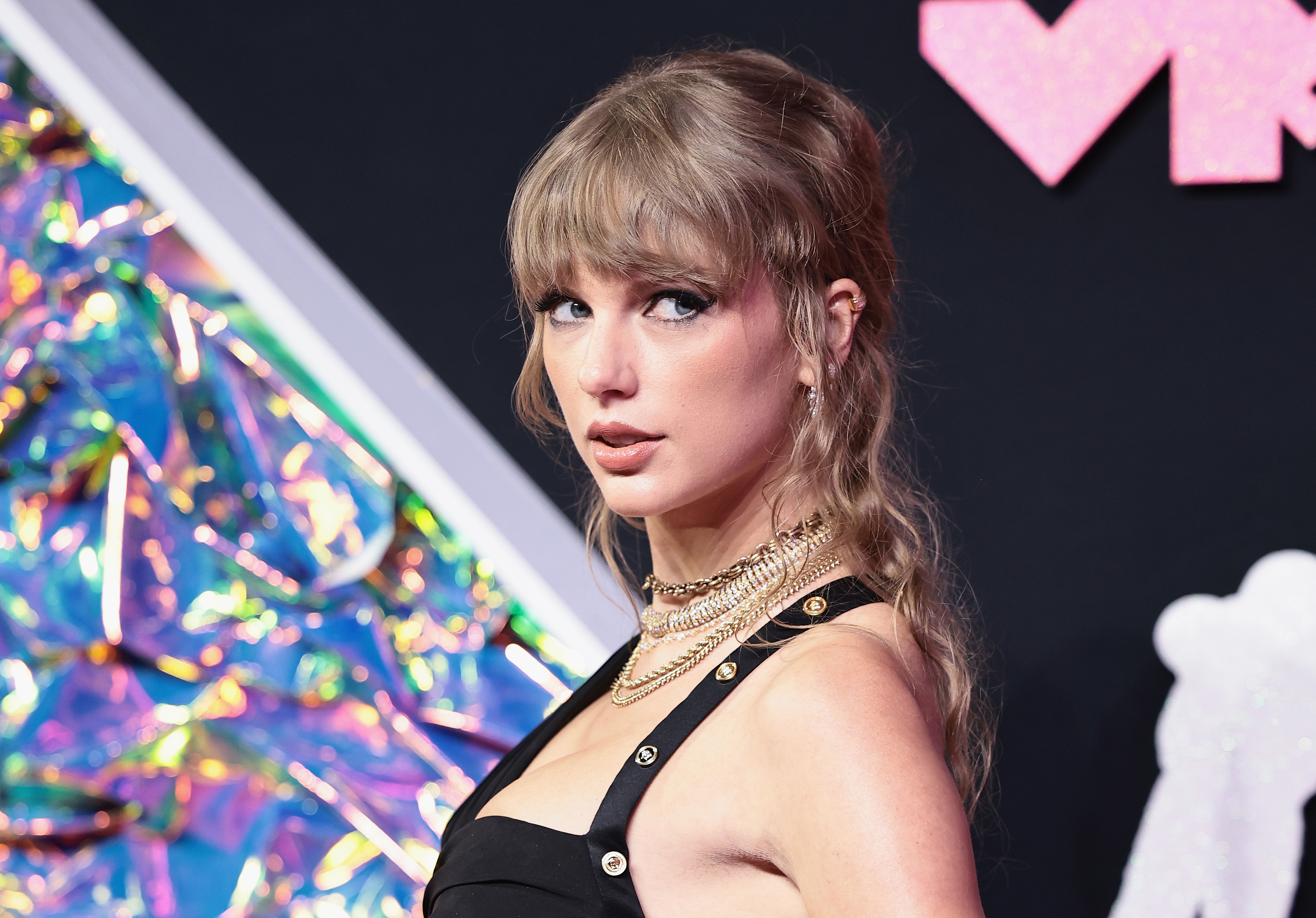 Taylor Swift at an event, wearing a black outfit with a gold chain necklace