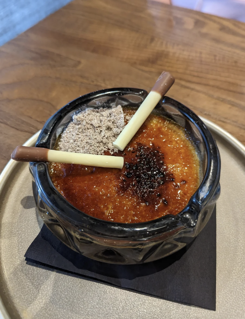 Creme brulee dessert in an ash tray garnished with two chocolate sticks on a tray
