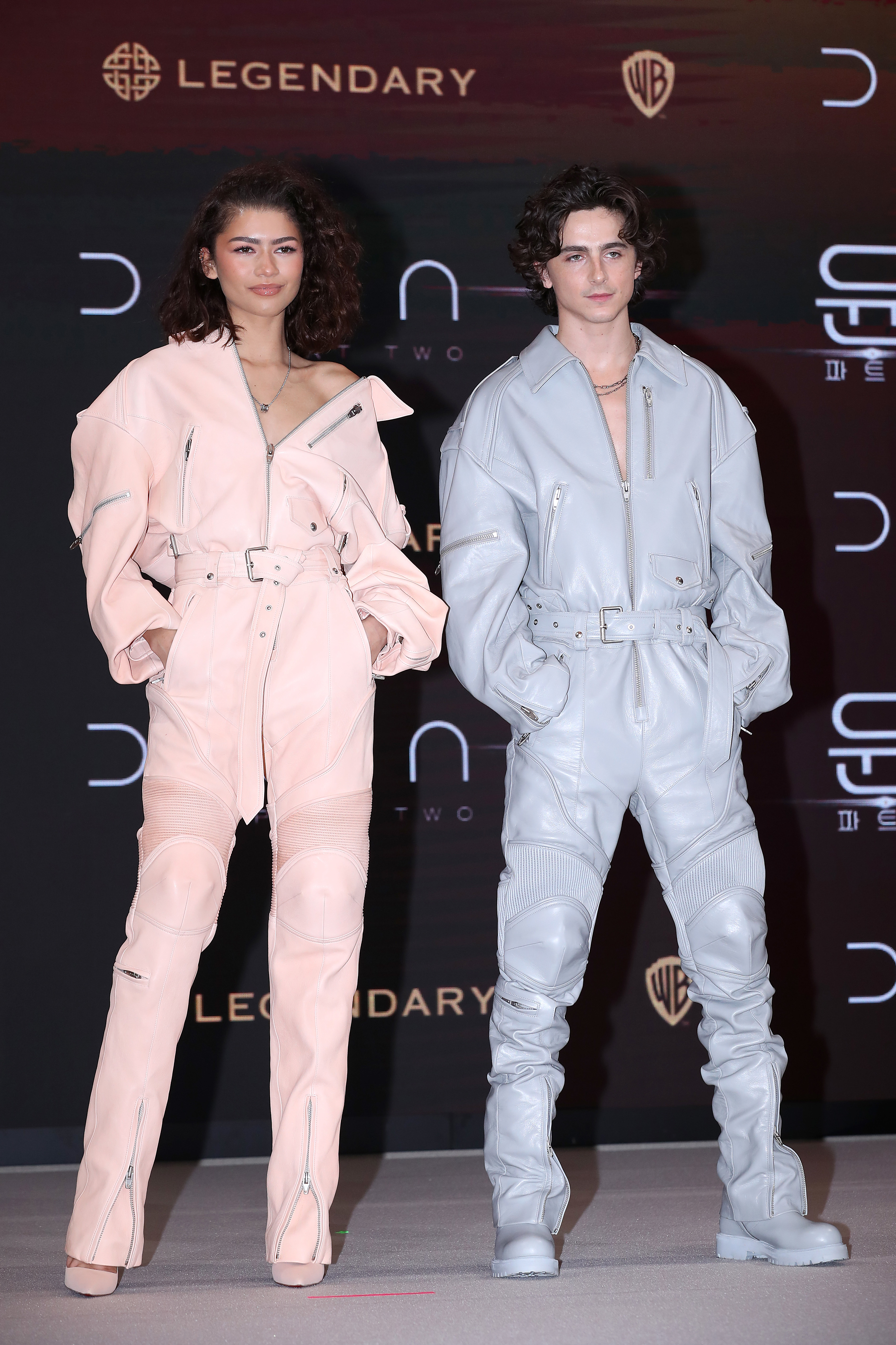 Zendaya and Timothée Chalamet at an event, both wearing stylish, monochromatic outfits and boots