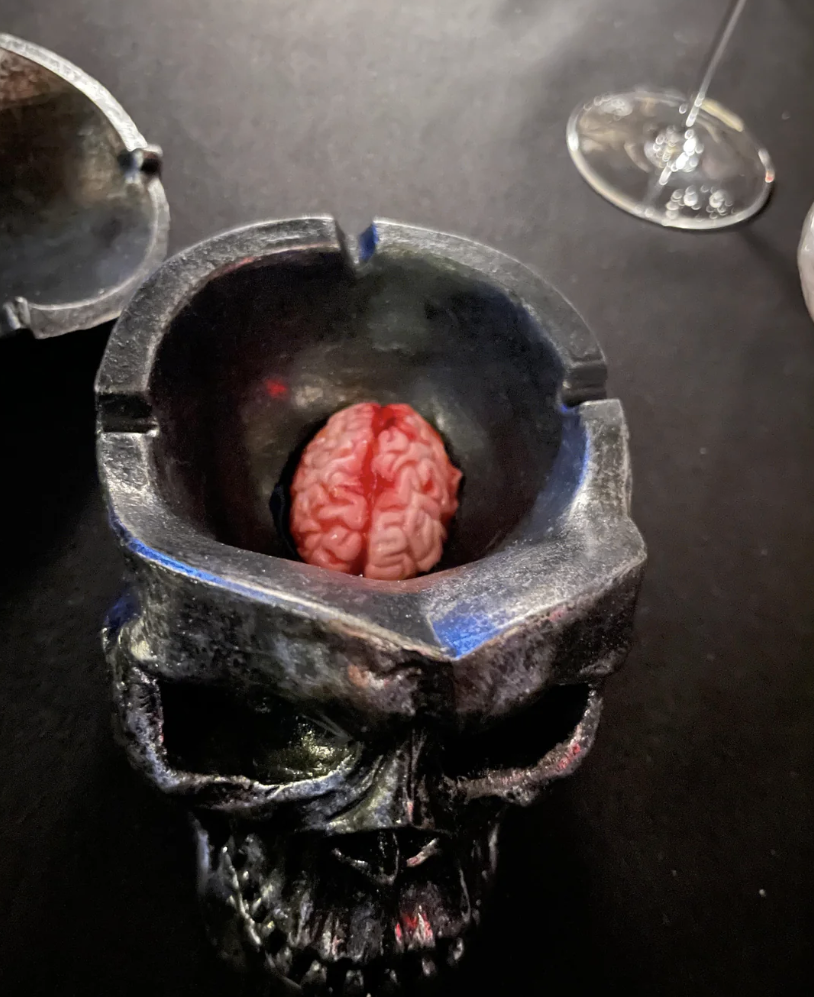 A brain-shaped dessert served in a skull-shaped bowl on a dark table, with a wine glass in the background