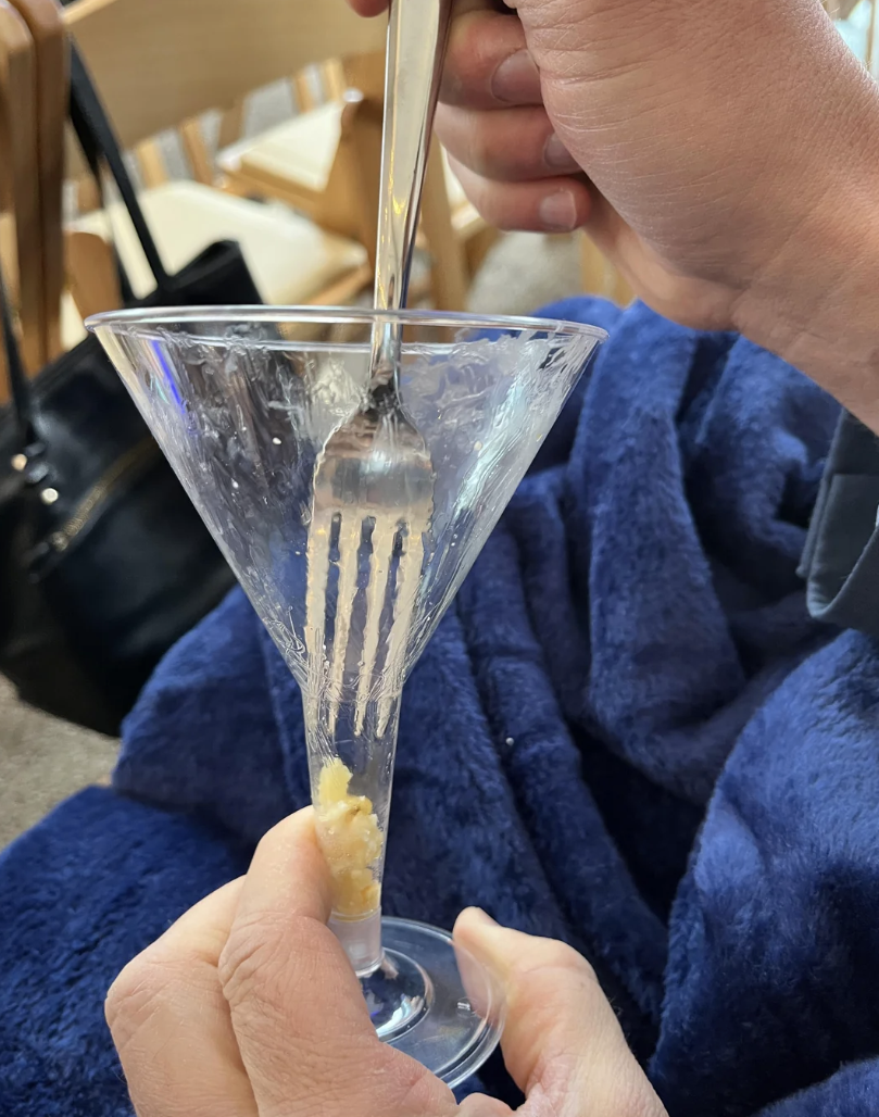 person trying to get their fork into the stem of a wine glass where mac and cheese has fallen