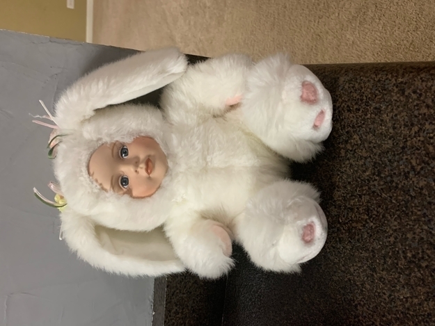 Plush toy resembling a baby with bunny ears and paws sitting on a surface