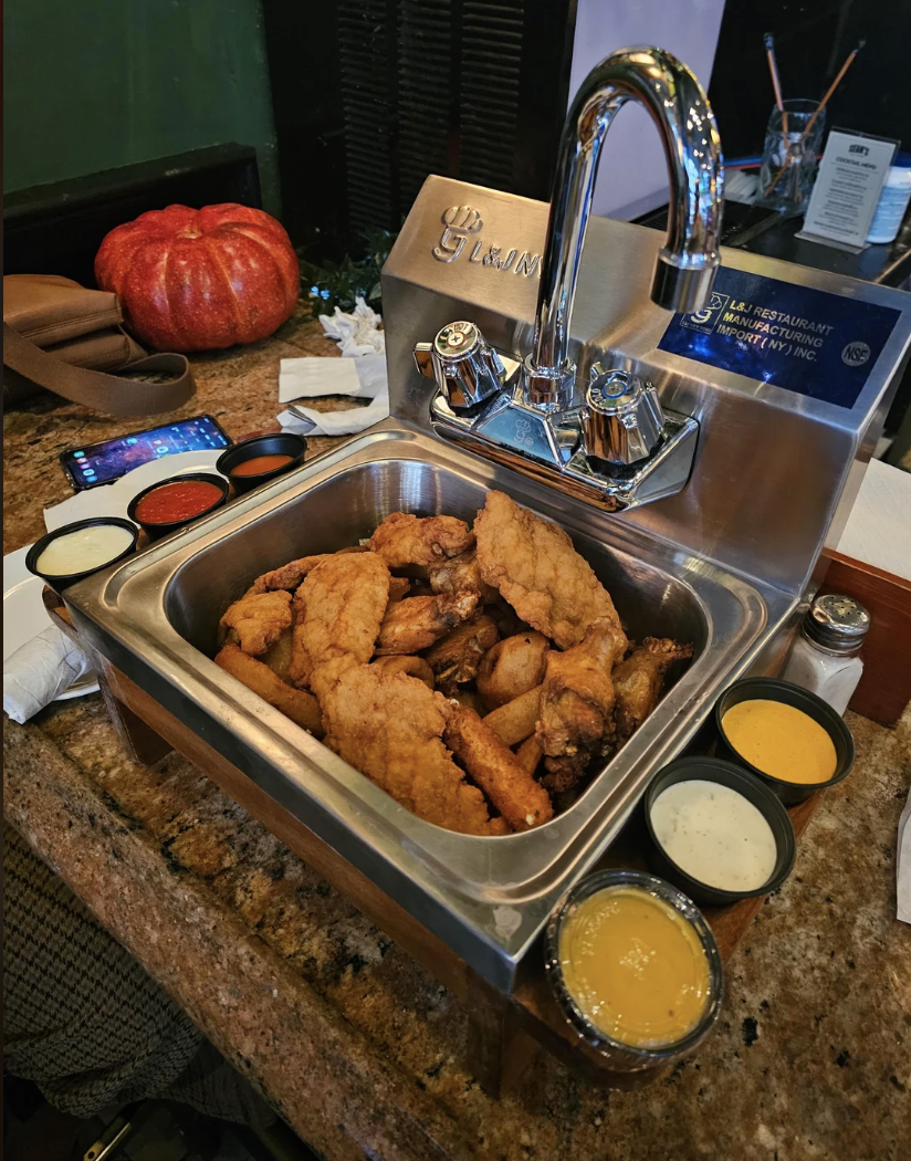 Sink filled with fried chicken, flanked by sauces, on a restaurant counter