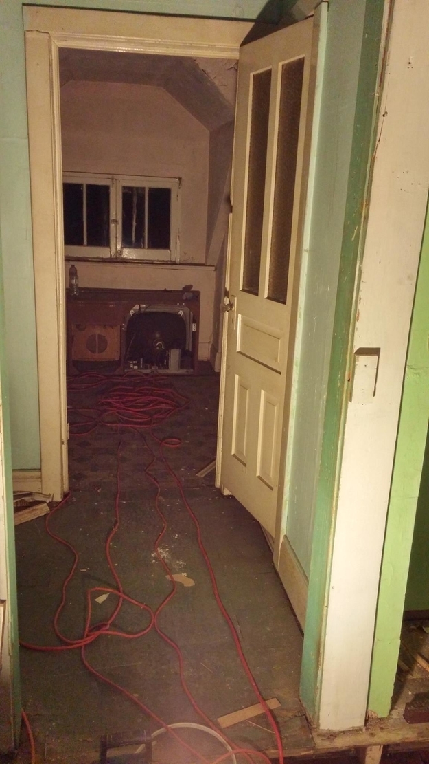 Interior of an old, dilapidated room with an open door and a red extension cord on the floor
