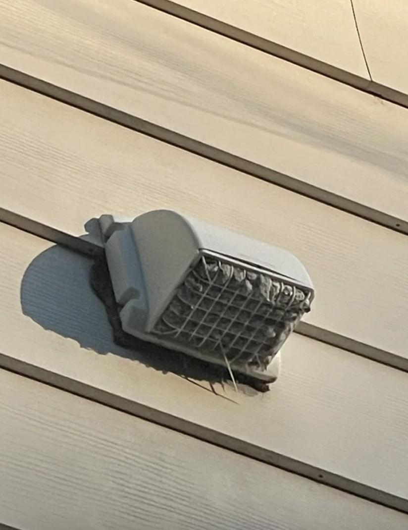 Exterior vent on a siding with a bird&#x27;s nest partially visible at the bottom