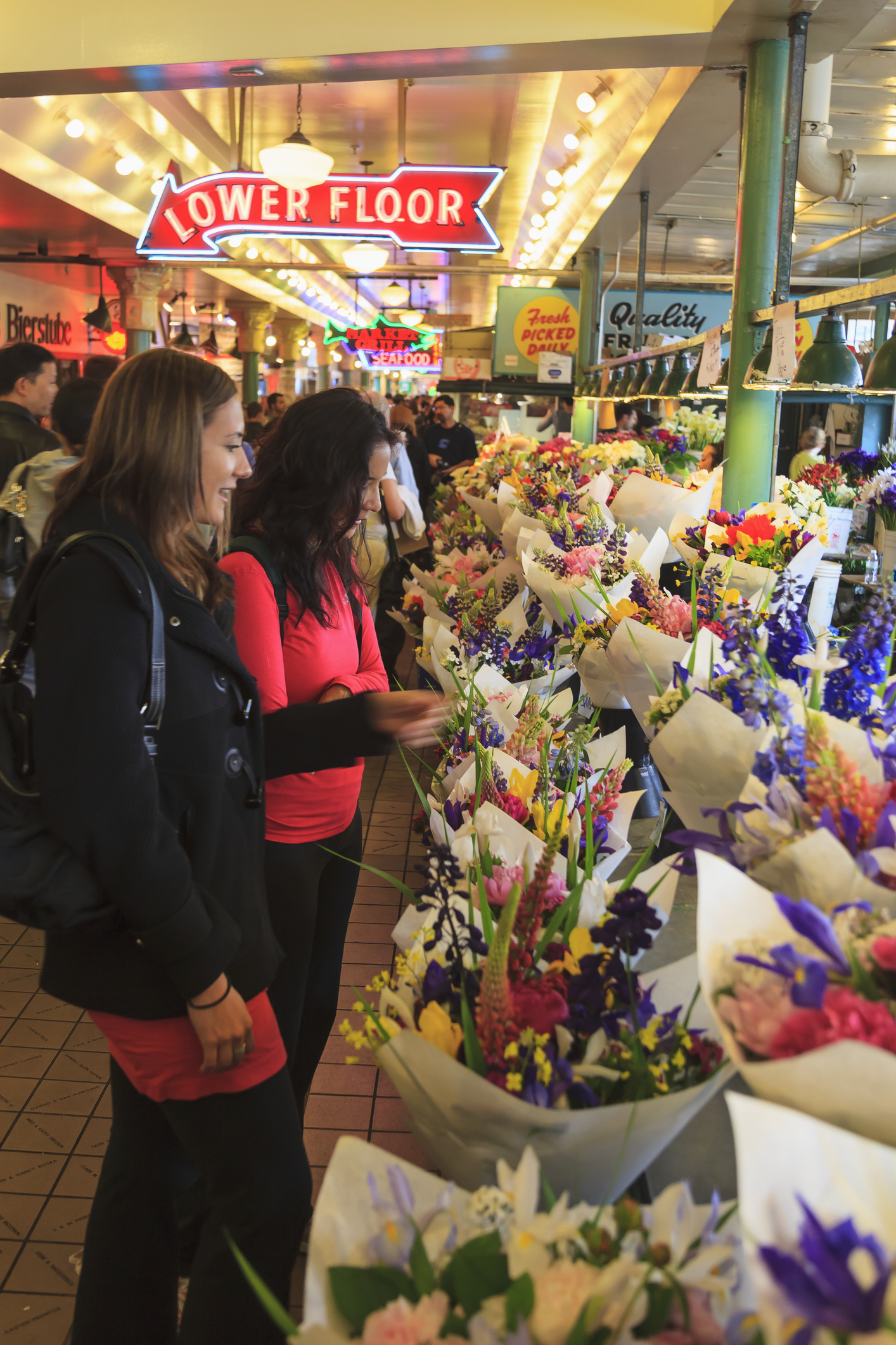 Two women browsing a vibrant flower market with assorted bouquets