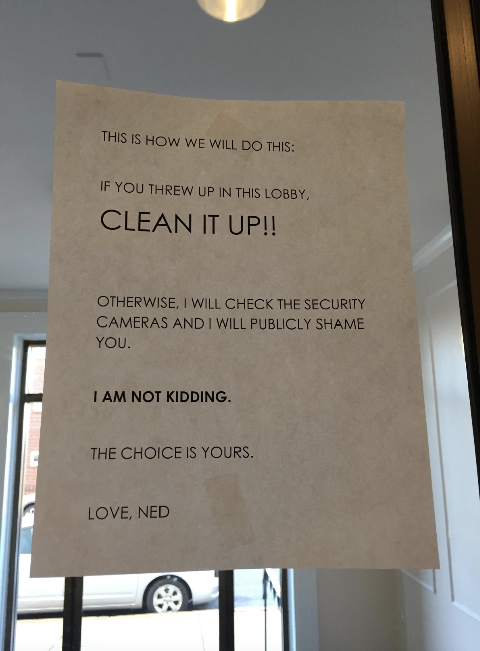 A stern warning sign taped to a door demands cleanliness in the lobby, threatening security camera review, signed by Ned