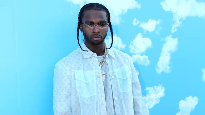 Pop Smoke stands against cloud backdrop, wearing a patterned shirt with layered chains