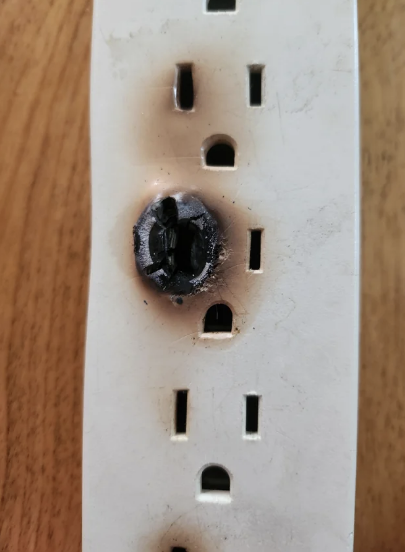 Burnt and damaged electrical outlet on a wall, posing a fire hazard