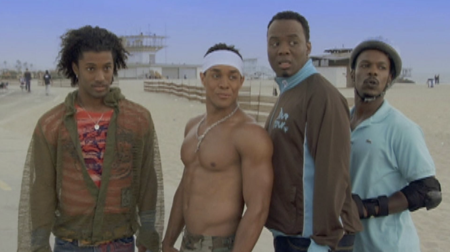 Noah&#x27;s Arc characters standing on a beach boardwalk, one shirtless, with a pier in the background