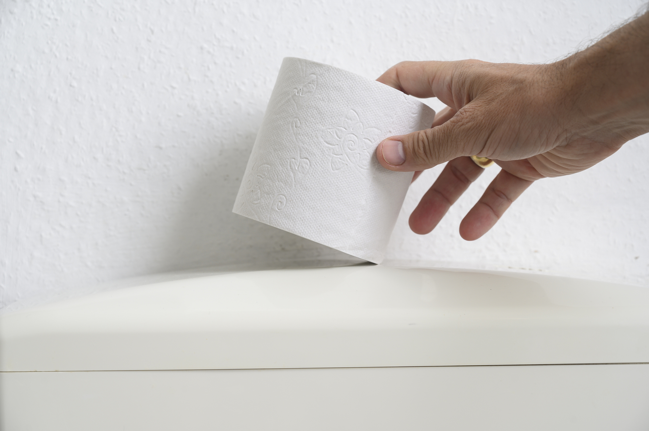 Hand grabbing toilet paper from the top of a toilet tank