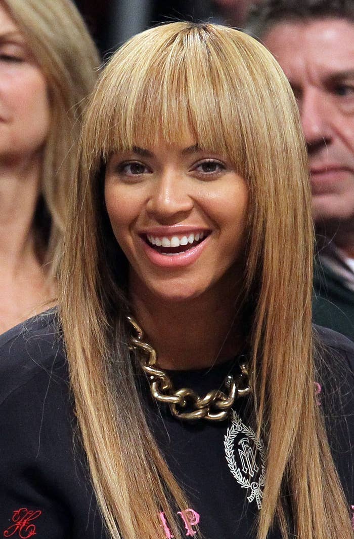 Close-up of Beyoncé smiling, wearing a black top with pink details and a gold chain necklace