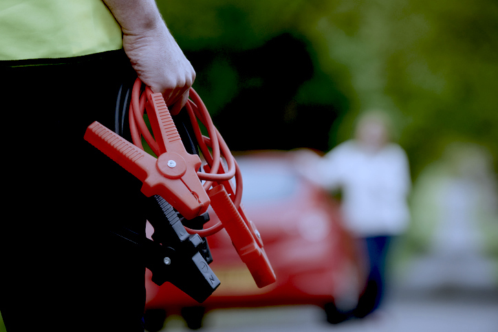 Person holding jumper cables with a blurred car and person in the background