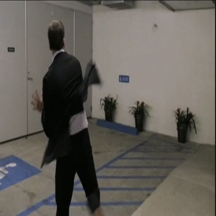 Man in a suit throwing a jacket while walking in a parking garage