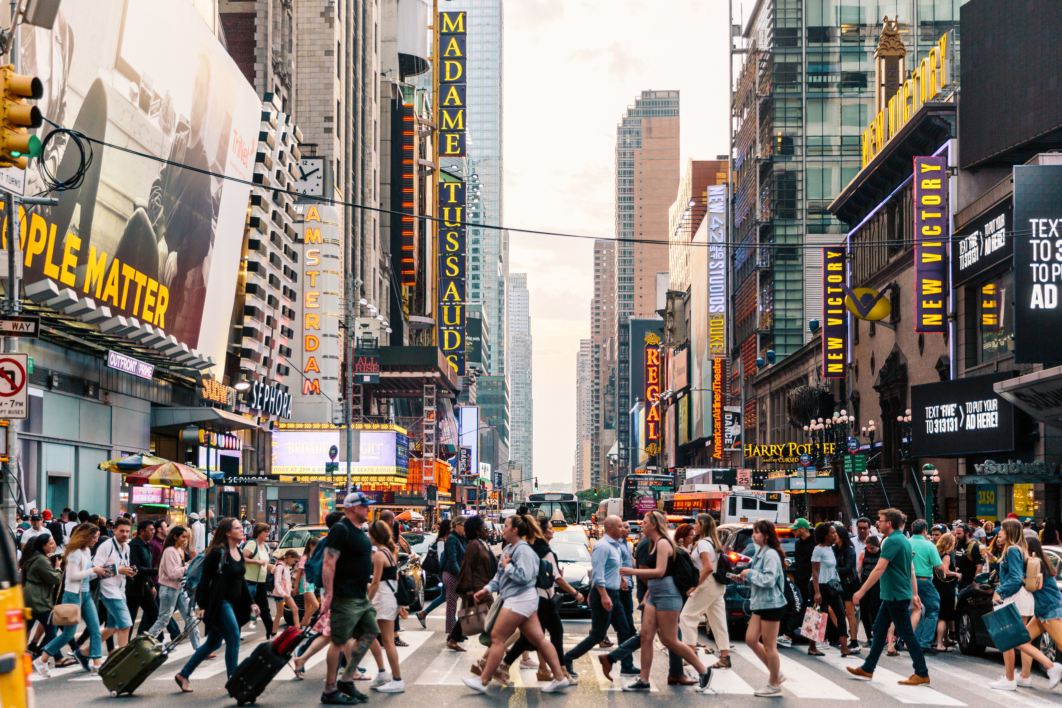 Pedestrians crossing a busy street in Times Square with billboards and buildings in the background