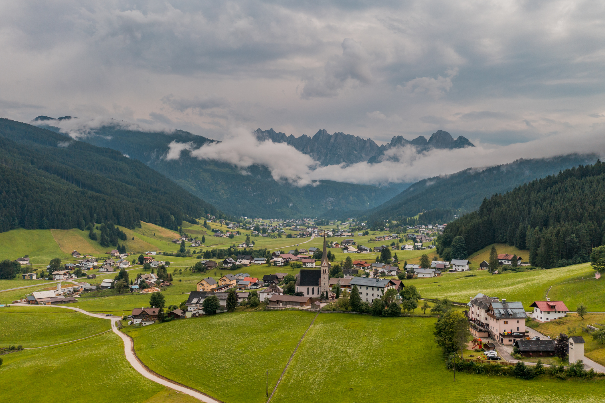 Aerial view of a village nestled in a valley with mountains partially obscured by clouds