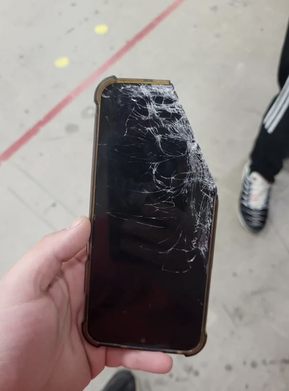 A person&#x27;s hand holding a smartphone with a severely cracked screen