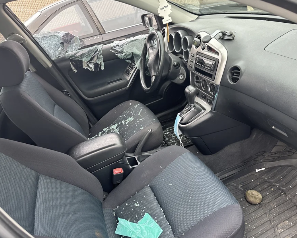 Car interior with shattered glass on seats and dashboard, airbags deployed, indicating an accident
