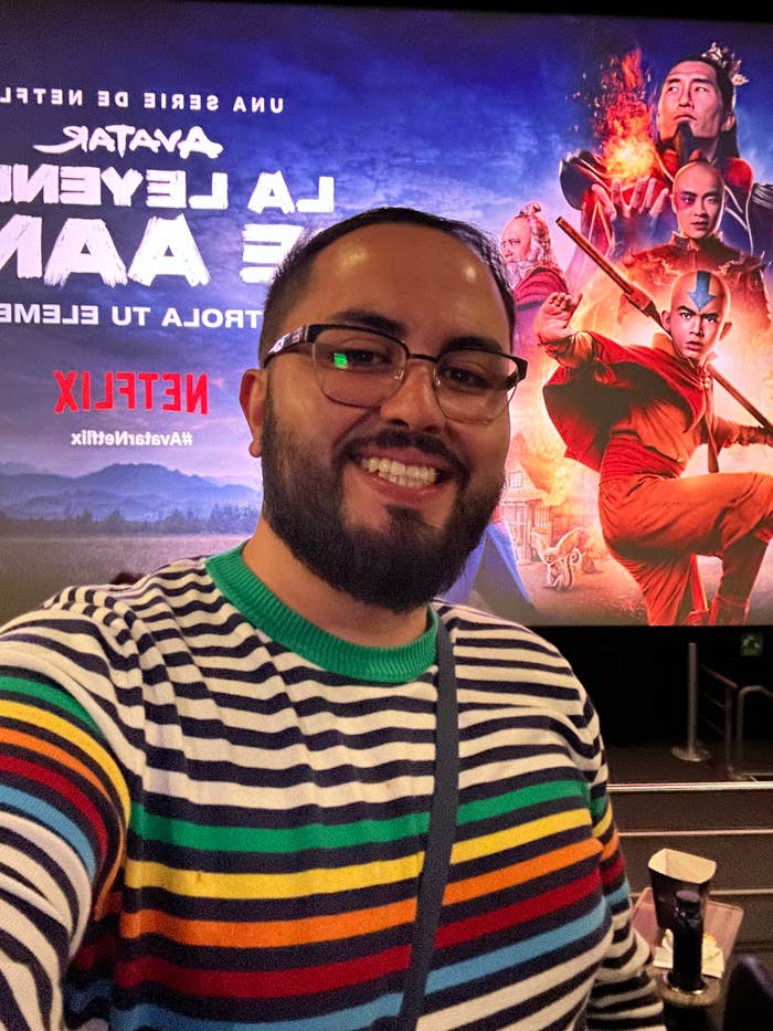 Person in striped sweater smiling in a cinema with an &#x27;Avatar: The Way of Water&#x27; poster in the background