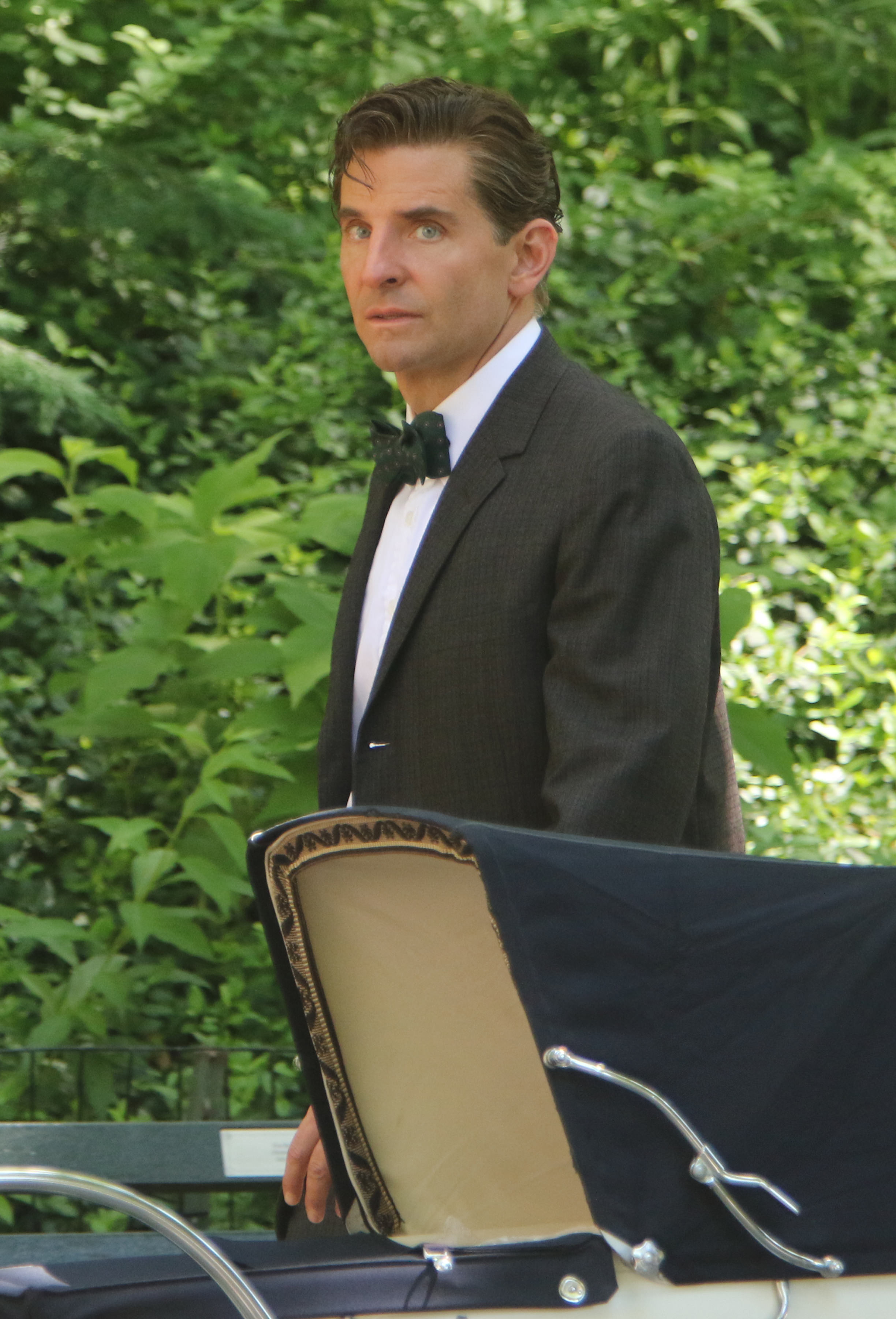 Man in a formal suit and bow tie looking over his shoulder next to a car