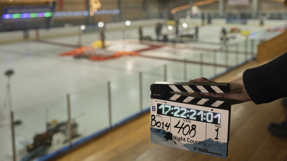 Clapperboard held in front of an ice rink with crew members preparing a scene