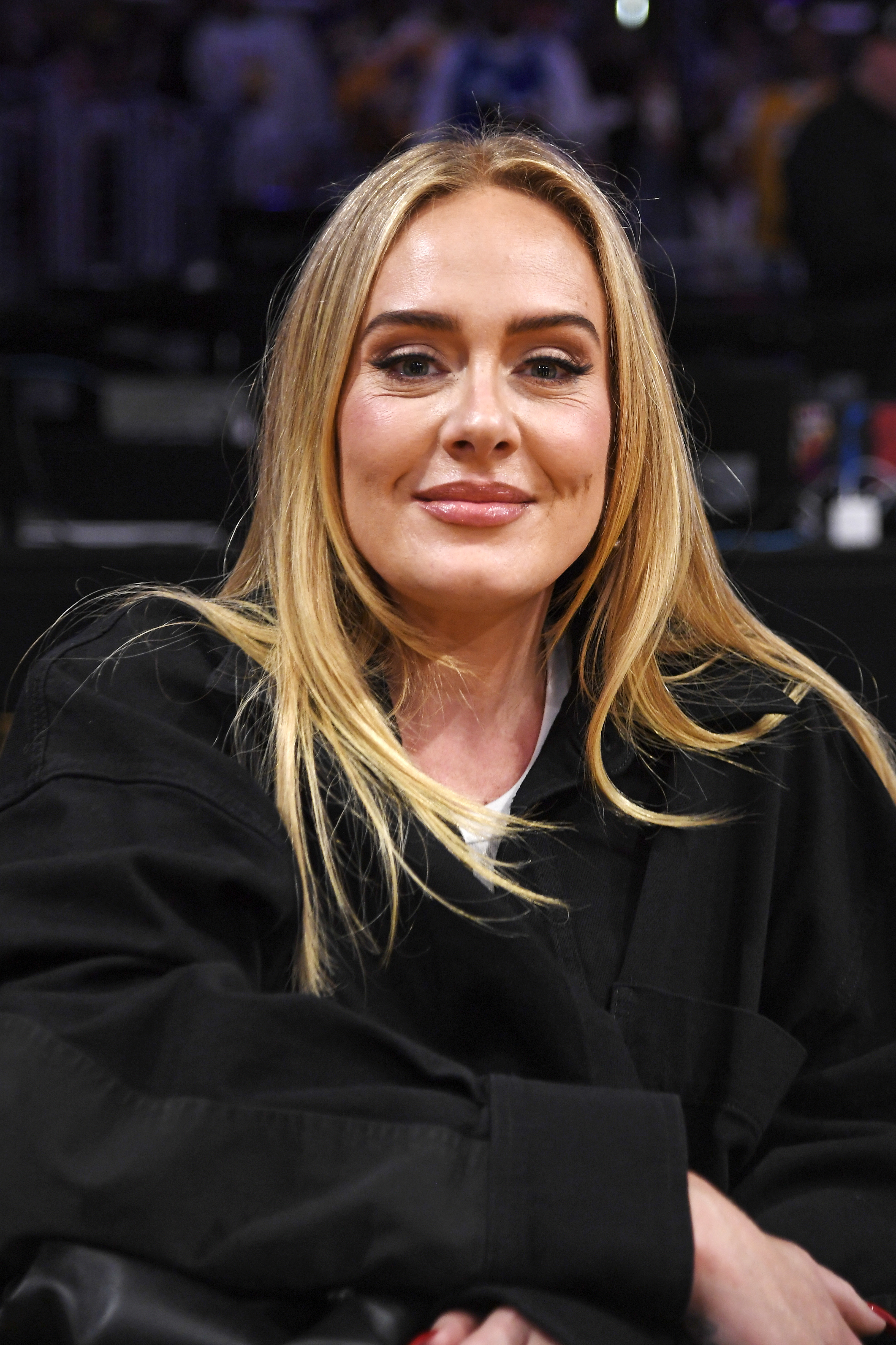 Adele seated at an event, smiling in a black top