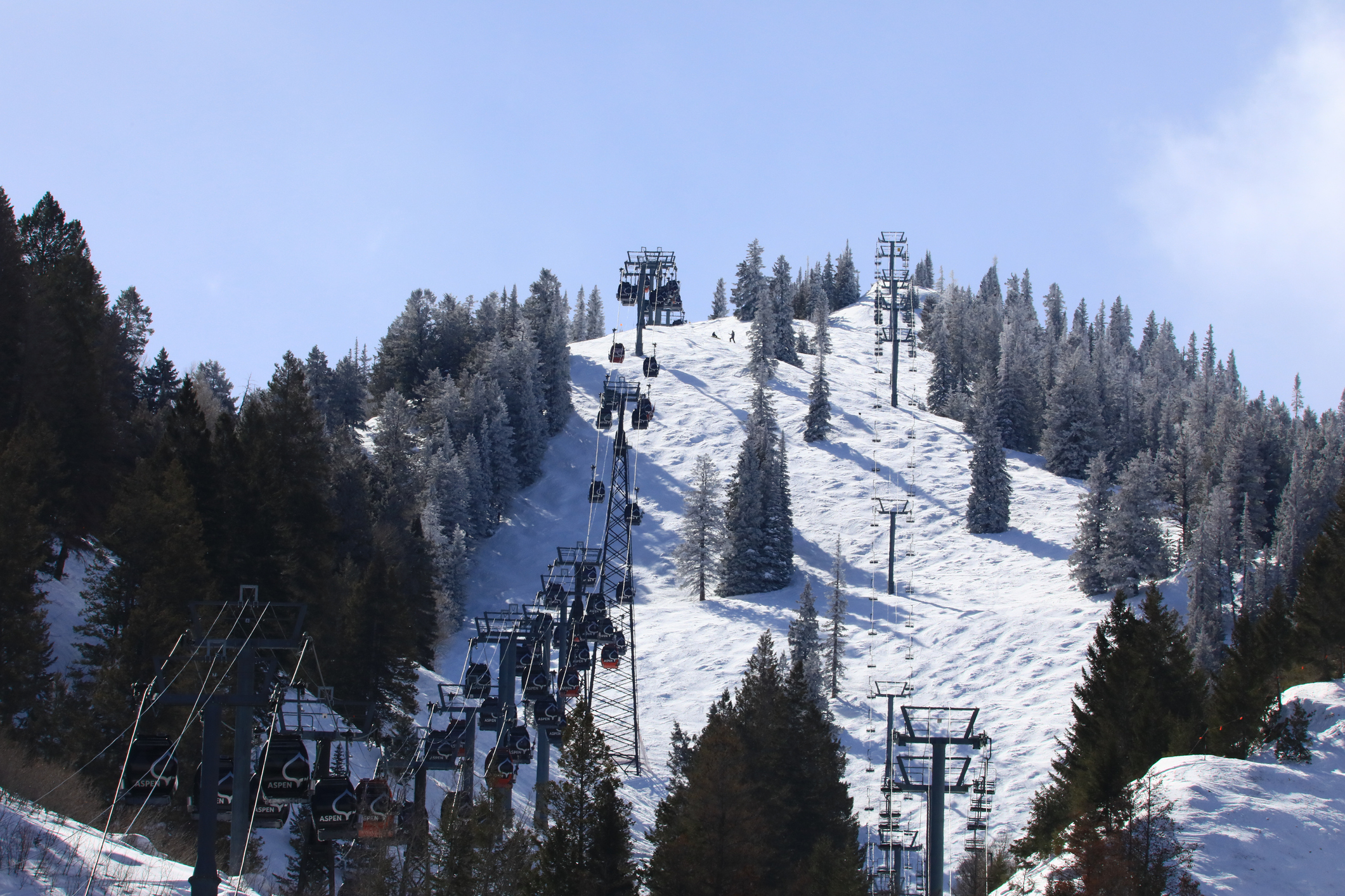 Ski lift with chairs ascending and descending a snowy mountain slope, surrounded by trees