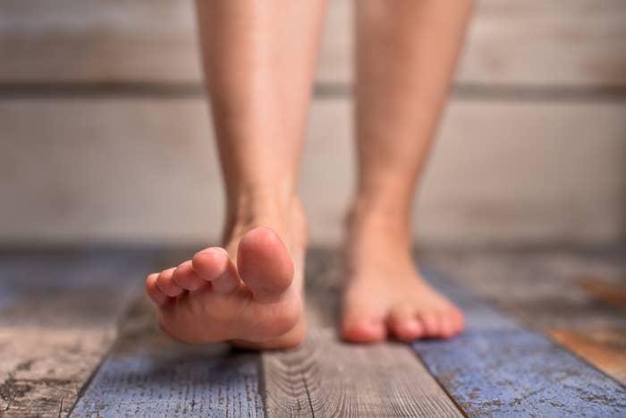 Close-up of a person&#x27;s bare feet stepping forward on a wooden floor
