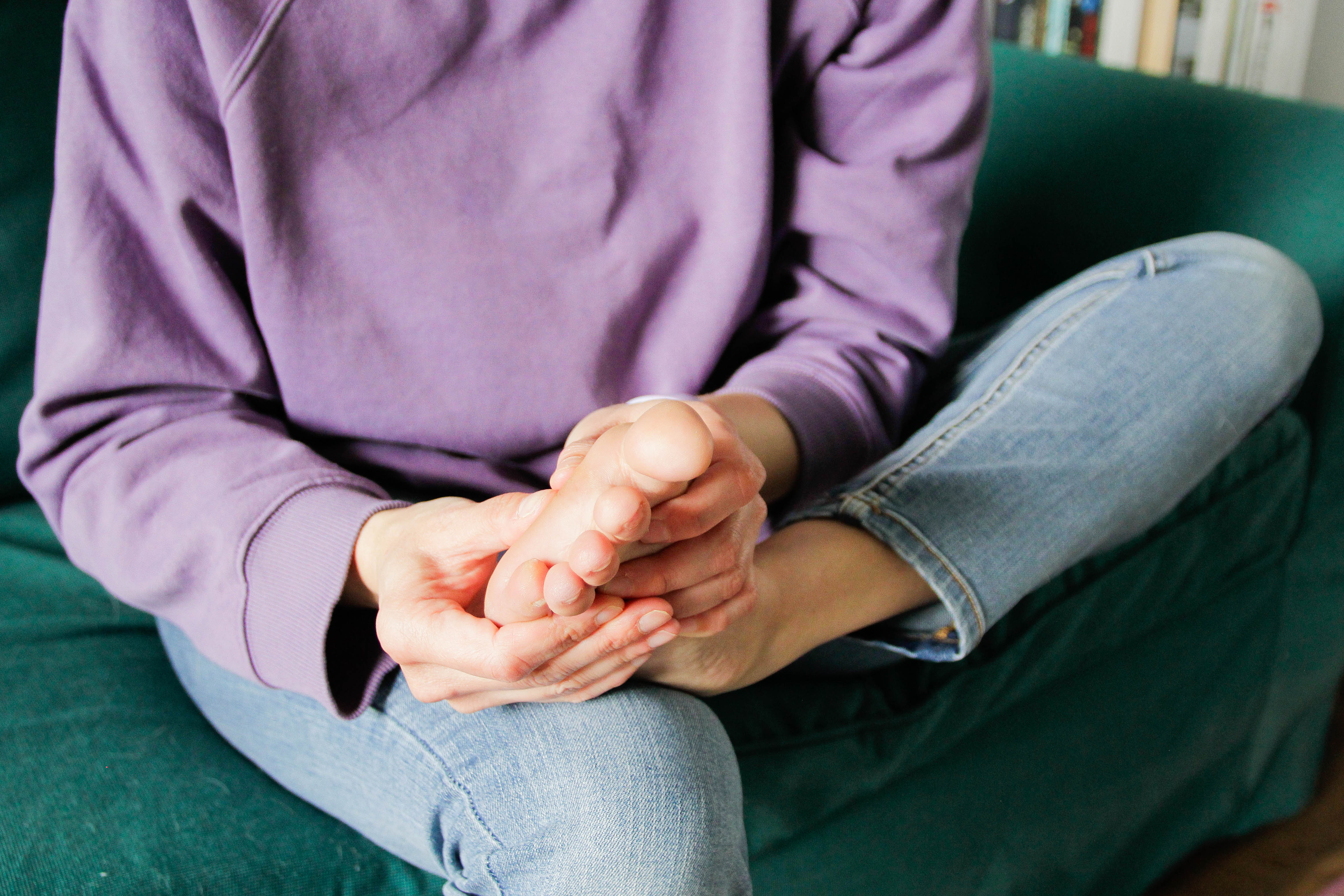Person sitting cross-legged on a couch, hands clasped together resting on their knees