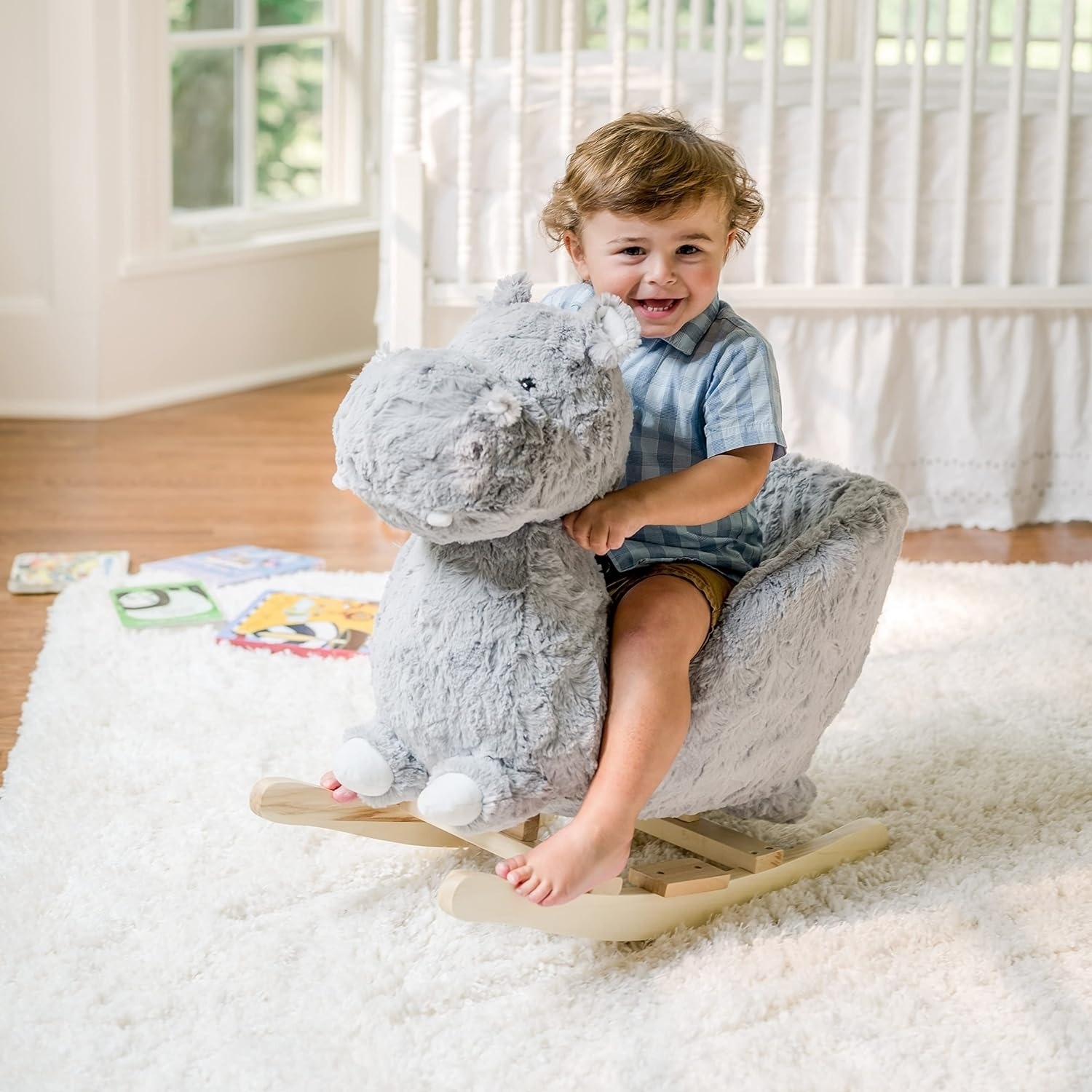 Child smiling on a plush hippo rocker toy in a home setting