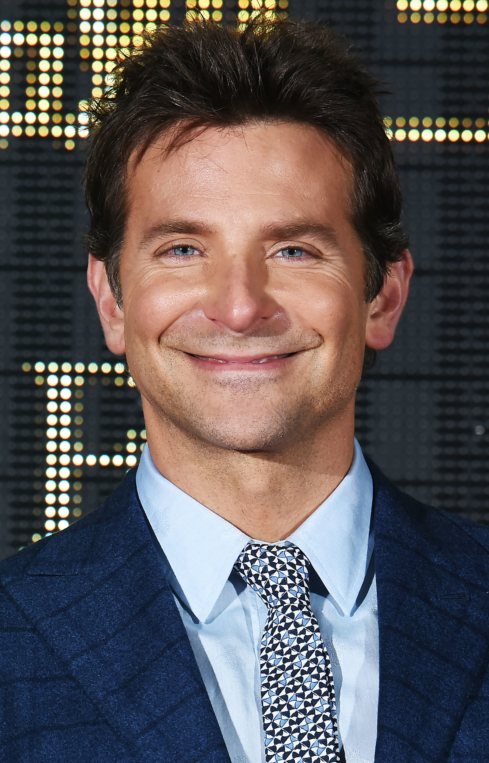 Bradley, in a patterned tie and blue suit jacket, smiling at a celebrity event