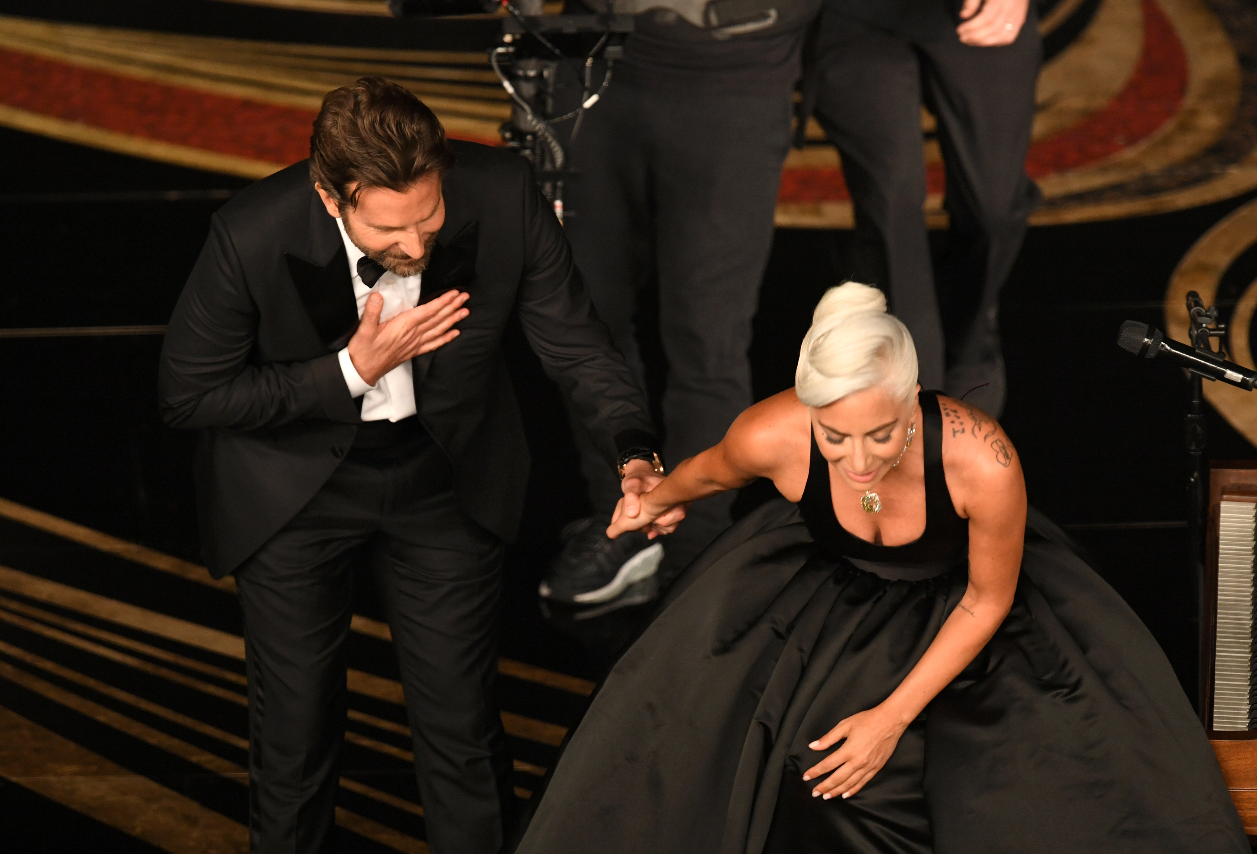 Bradley, in a bow tie and suit, helps Gaga in a black gown up the stairs to the stage