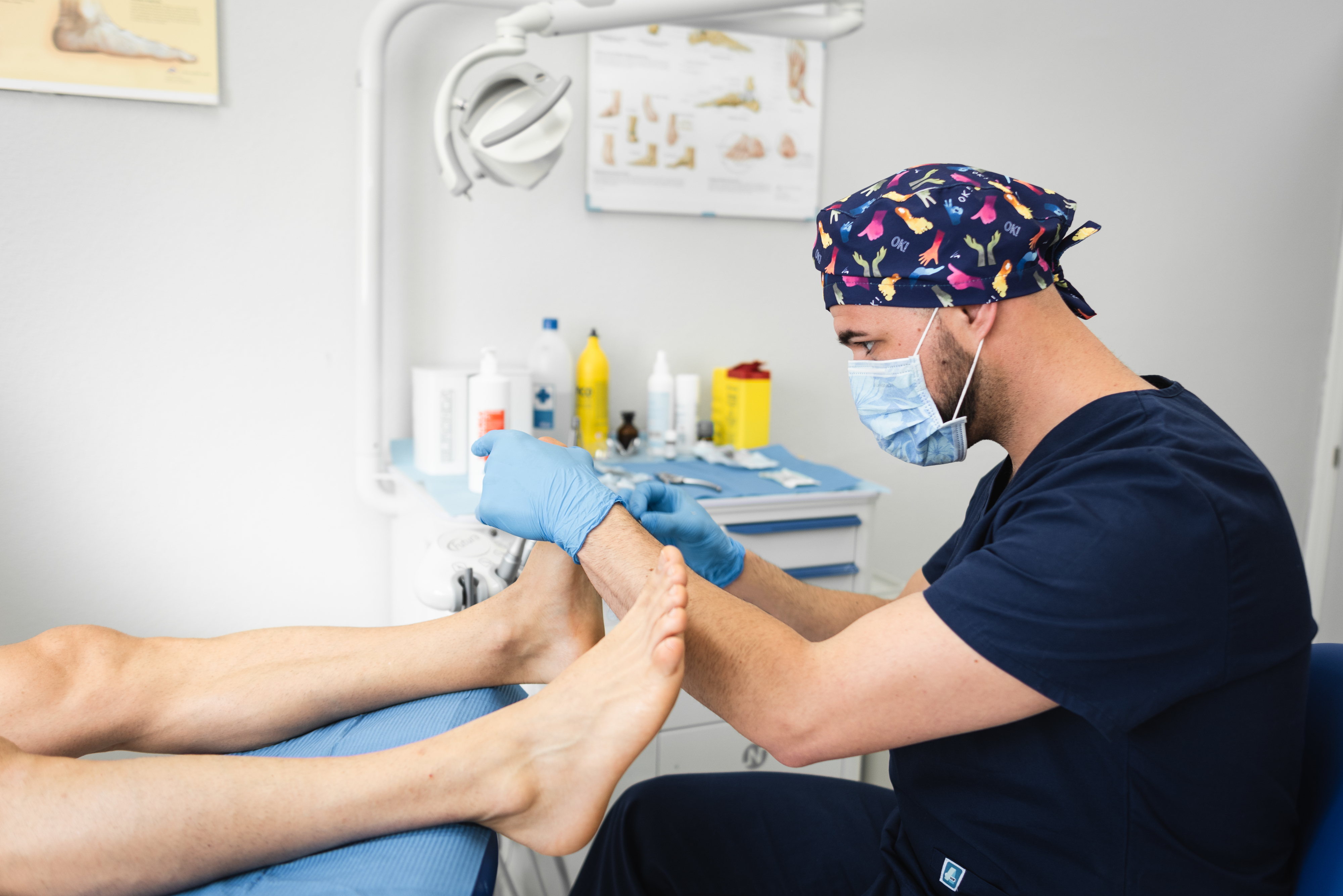 A podiatrist in scrubs examines a patient&#x27;s foot in a clinic