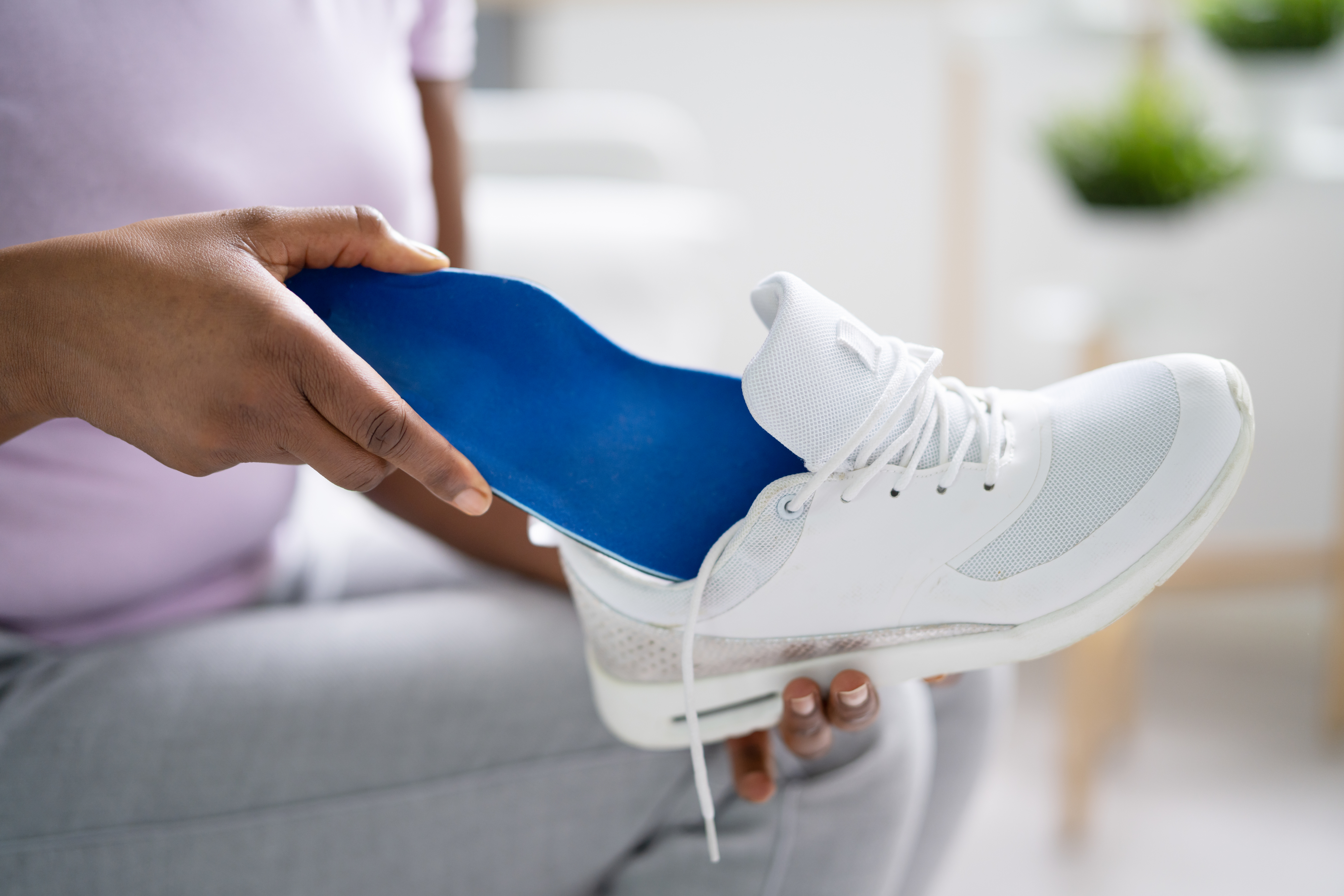 Person inserting an orthopedic insole into a white sneaker