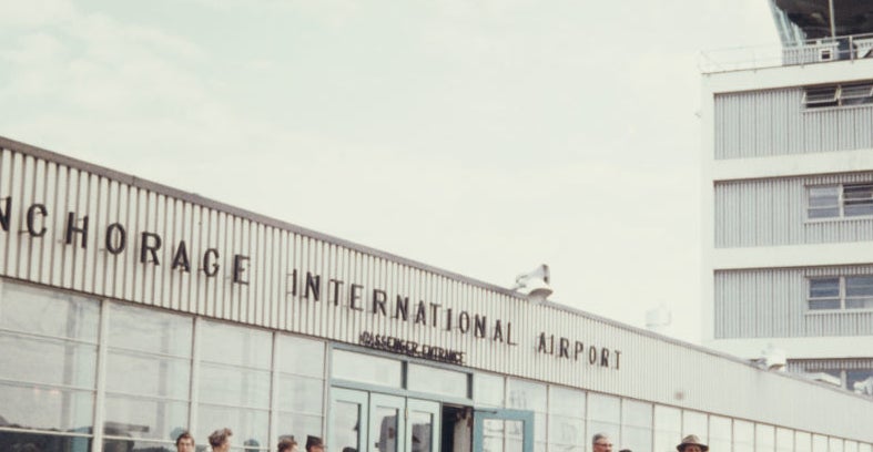 Group of people standing outside the Anchorage International Airport in a historical photo