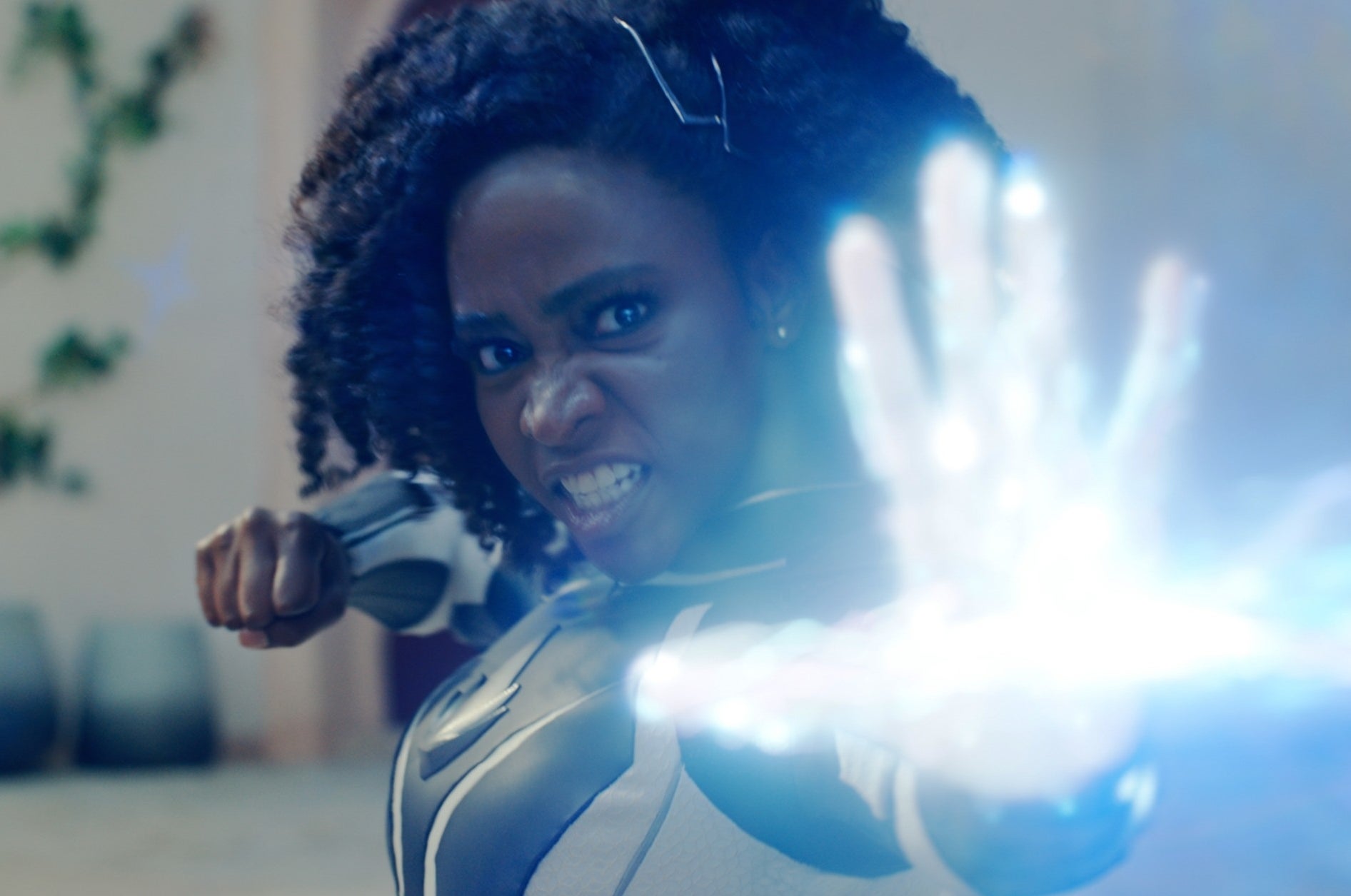Monica in a superhero costume with a focused expression using powers emitting blue light from hand
